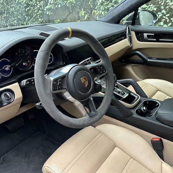 Porsche Cayenne steering wheel in gray Alcantara with a yellow 12 o'clock marker and yellow stitching, in a cream interior